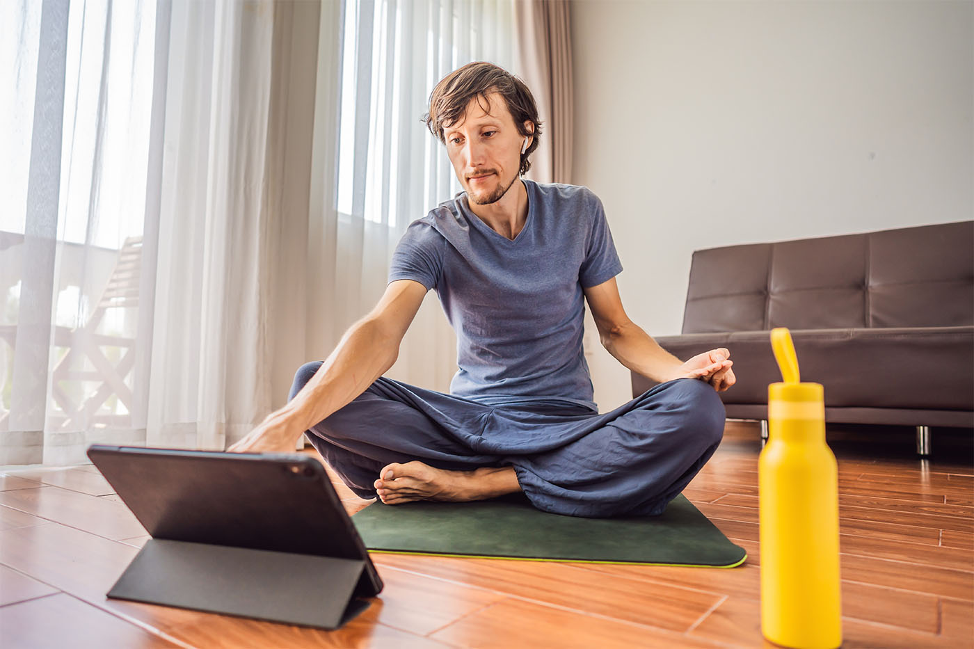 Fitness man exercising on the floor at home and watching fitness videos in a tablet. People do sports online because of the coronovirus