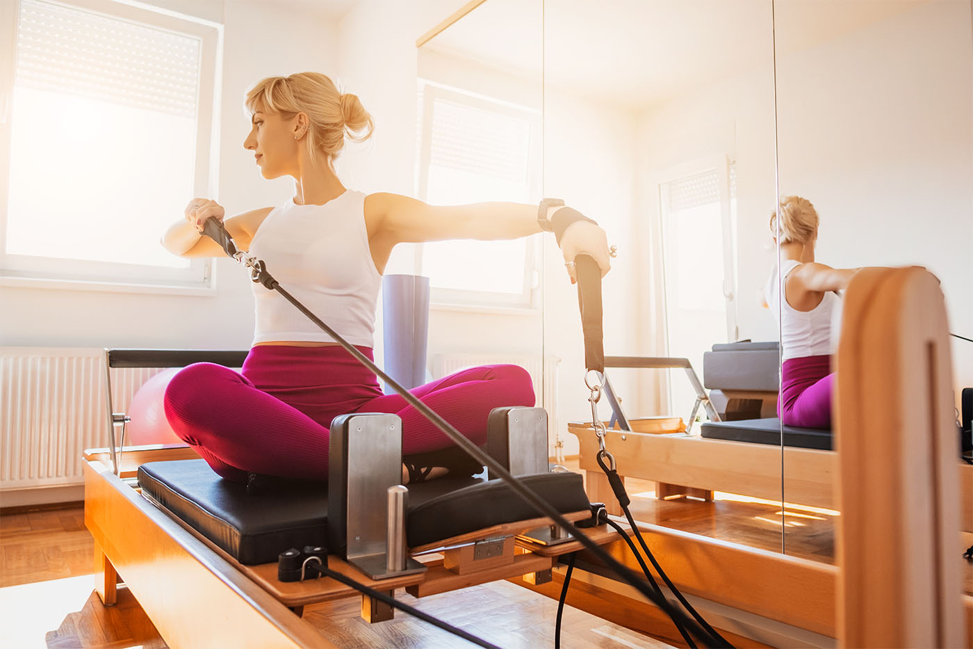 Woman is exercising on pilates reformer bed in her home.
